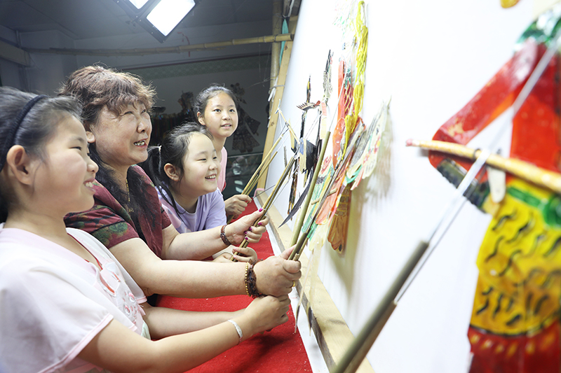 皮影藝人指導(dǎo)小朋友表演皮影戲。